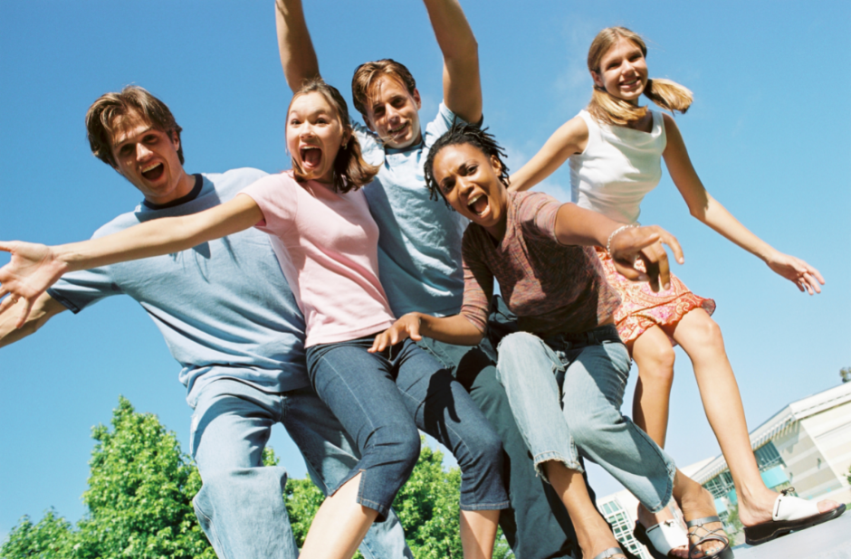 A stock image of a group of teens looking down and smiling at a camera.