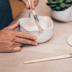 An up close image of a person painting a ceramic pot.