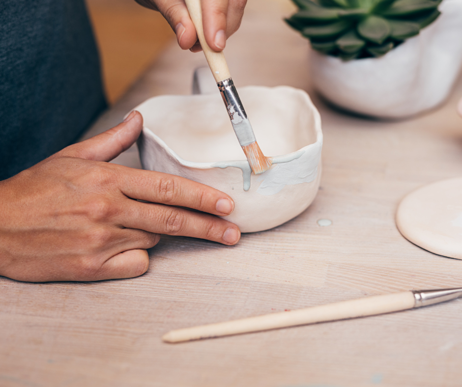 An up close image of a person painting a ceramic pot.